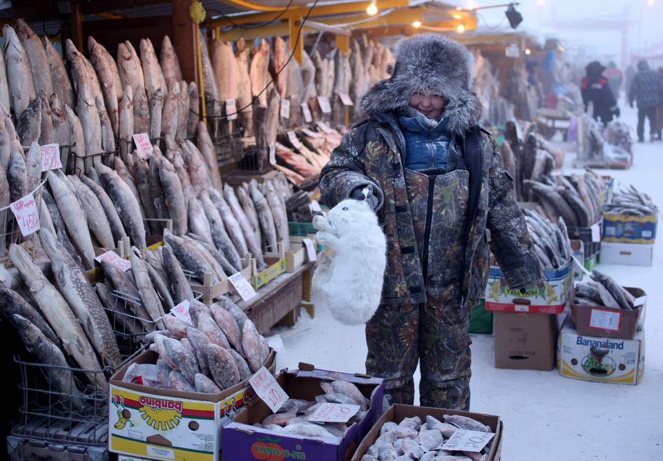 ein Verkaufsstand auf dem markt mit gefrorenen Fischen. Die Marktfrau hält einen Hasen in der Hand.