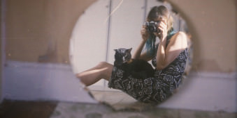 Eine Frau mit schwarzer Katze auf dem Schoss schließt ein Foto in einen Spiegel.