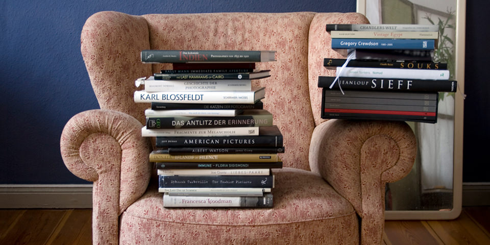 Ein Stapel Foto-Bücher und Bände sitzen auf einem älteren Sessel.