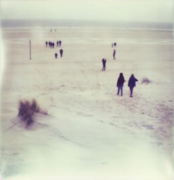 Menschen laufen an einem Strand auf das Meer zu.