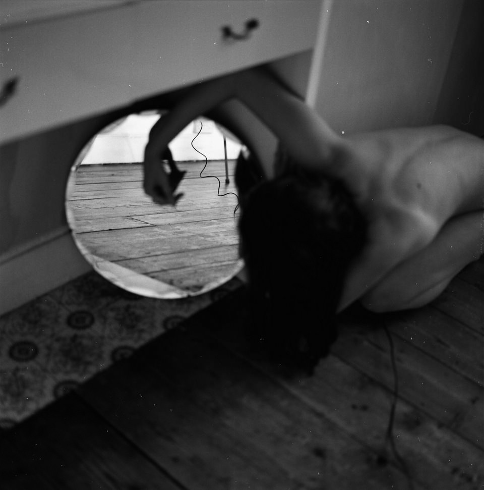 Eine nackte Frau beugt sich seitlich um einen Spiegel herum.