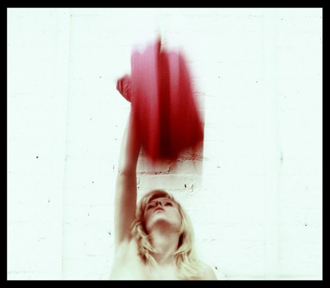 Eine Frau wirft vor einer weißen Wand ein rotes Tuch in die Höhe.