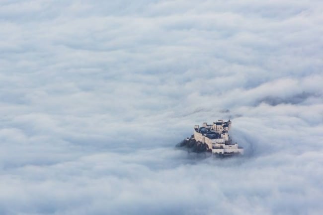Ein Schloss ragt aus einem Wolkenmeer.