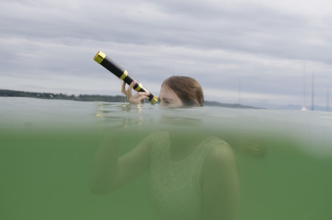 Eine Frau schaut mit einem Fernglas aus dem Wasser