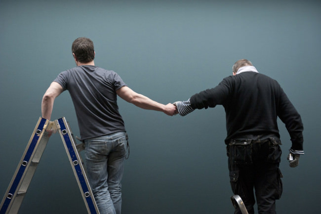 Ein Mann auf der leiter hält die Hand eines anderen Mannes.