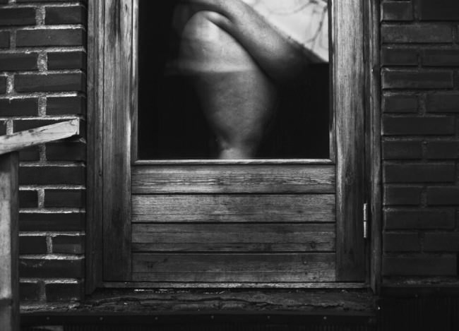 Nackte Frau steht hinter einem Fenster.