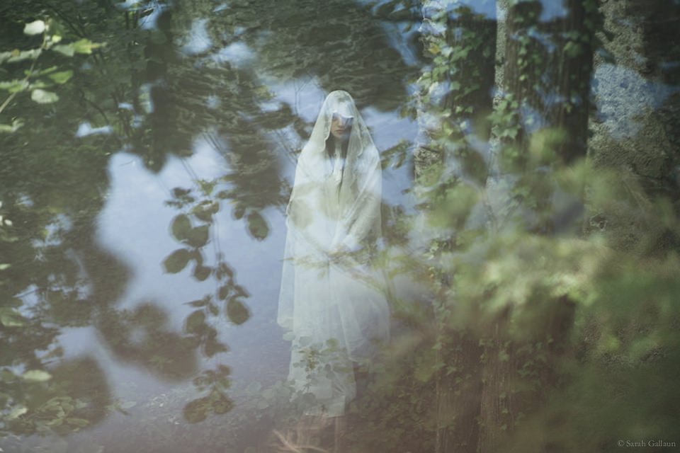 Eine Frau in weißem Kleid im Wald, überlagert von Spiegelungen.