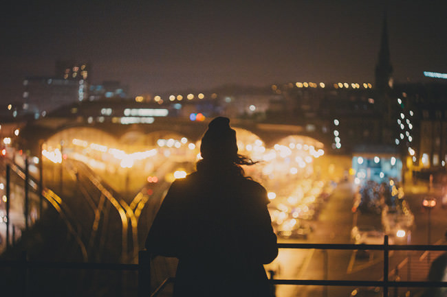 Eine Person steht auf einer Brücke und schaut auf eine erleuchtete Stadt herunter.