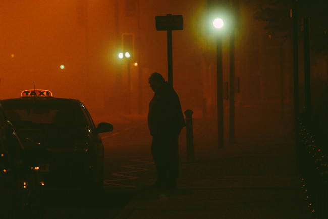 Silhouette eines Mannes, der in diesigem Licht neben einem Taxi am Straßenrand steht.