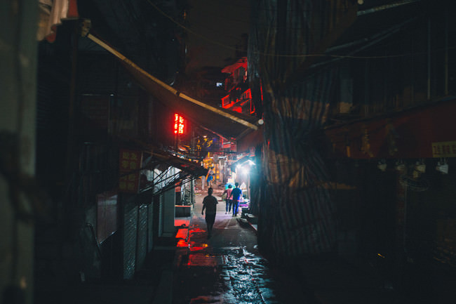 Menschen in einer verbauten Gasse einer asiatischen Stadt.