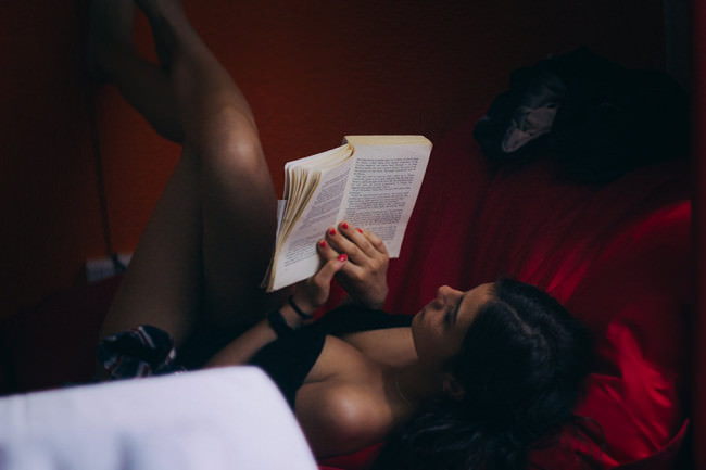 Eine Frau liegt in Unterwäsche auf einem roten Sofa und liest in einem Buch.