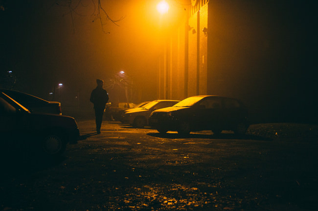 Eine Person geht im Dunkel über einen nebligen Parkplatz.