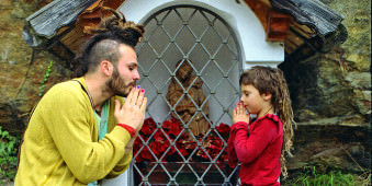 Ein Mann und ein Mädchen beten vor einem bunten Altar.
