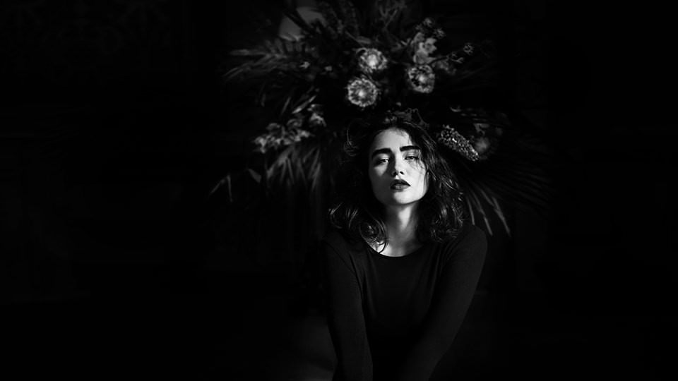 Frauenportrait vor einem Blumenstrauß und dunklem Hintergrund.