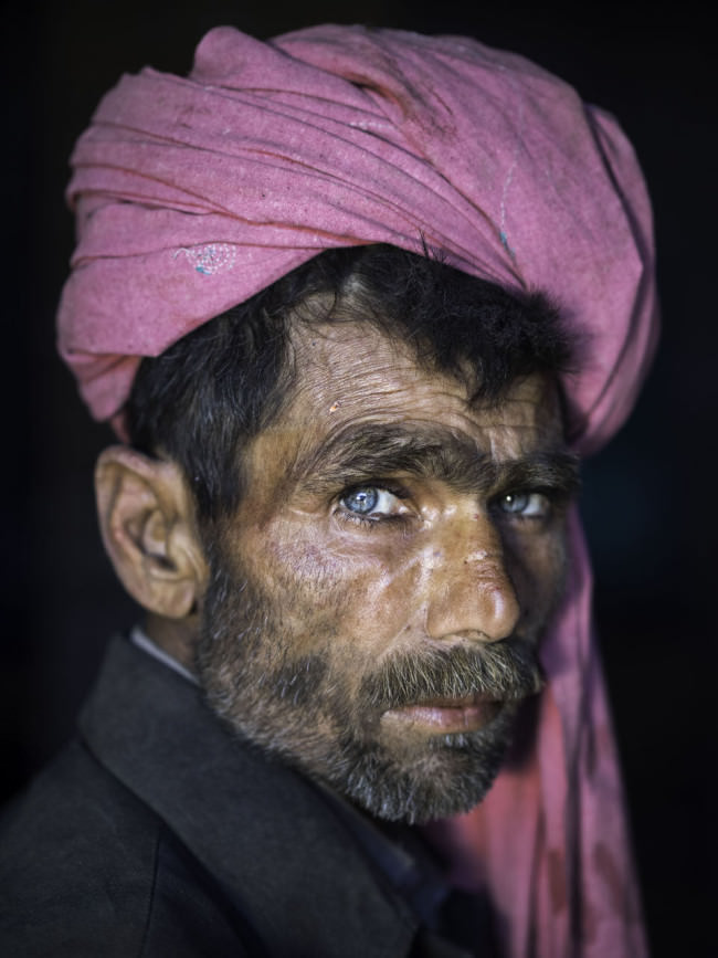 Ein Mann mit tiefblauen Augen und rosarotem Turban schaut in die Kamera. 