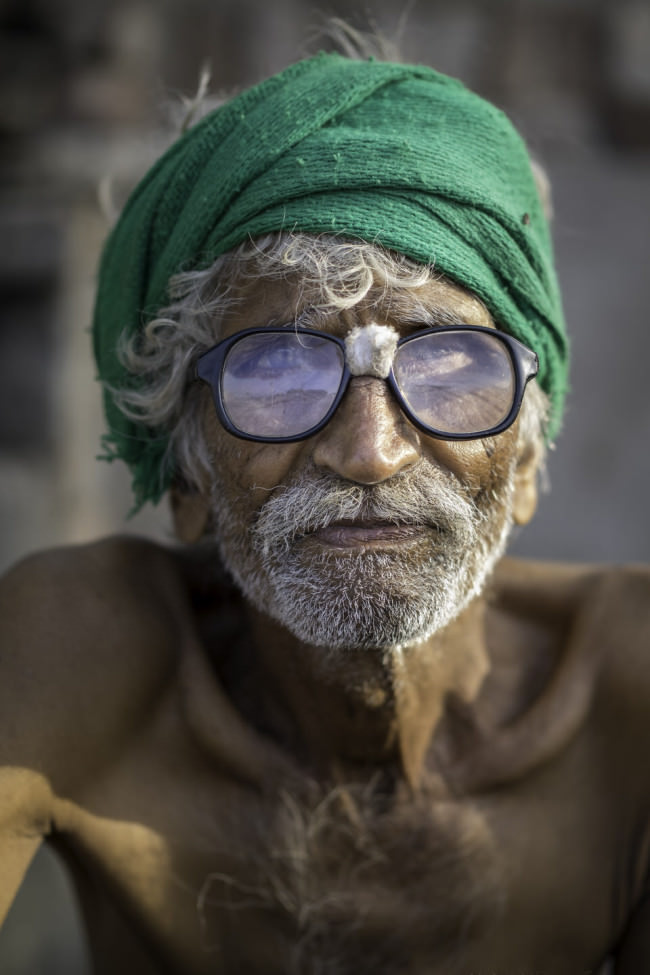 Ein Mann mit grünem Turban und starker Brille schaut in die Kamera. 