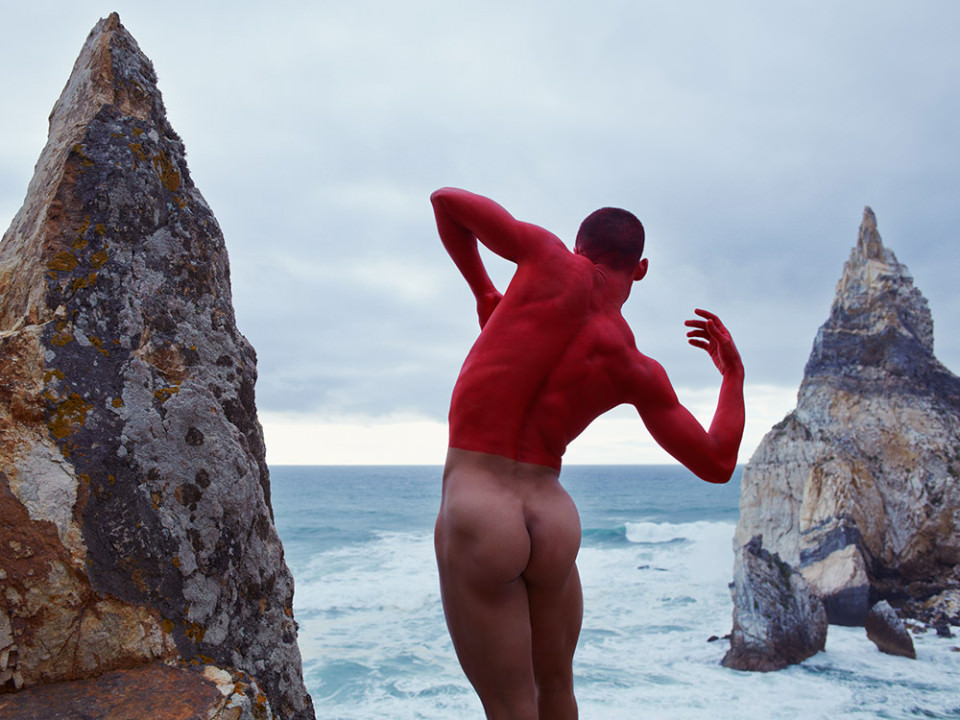 Ein Mann mit rotem Oberkörper am Strand zwischen Felsen.