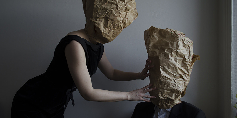 Zwei Personen mit Papiertüten auf dem Kopf beugen sich zueinander..