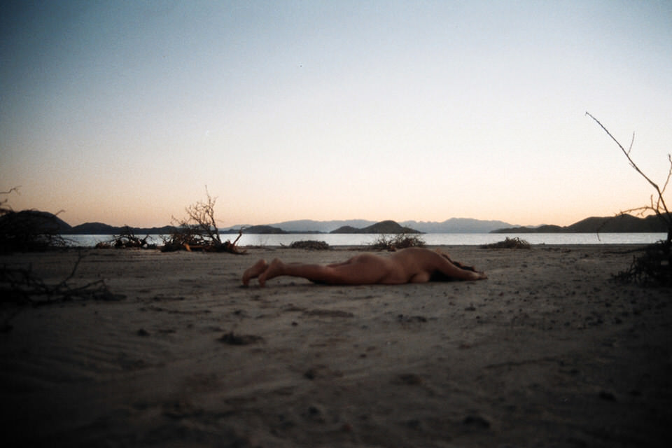 Eine Frau liegt mit dem Gesicht nach unten im Sand vor dem Meer.