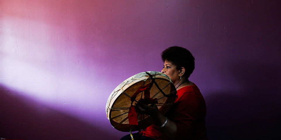 Eine Frau mit Trommel vor einer lilanen Wand.