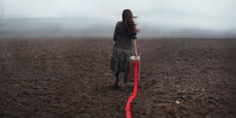 Ein Mädchen läuft über einen nebeligen Acker und zieht ein rotes Band hinter sich her.