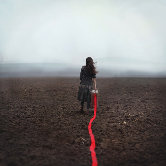 Ein Mädchen läuft über einen nebeligen Acker und zieht ein rotes Band hinter sich her.