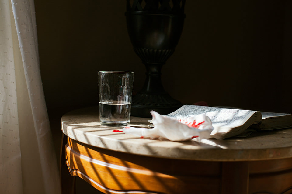 Ein Nachtisch mit einem Glas Wasser, einem Buch und einem Taschentuch mit roten Flecken.