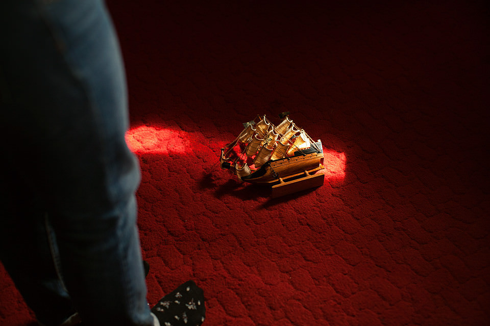 Ein Modellschiff liegt im Lichtschein auf einem roten Teppich.