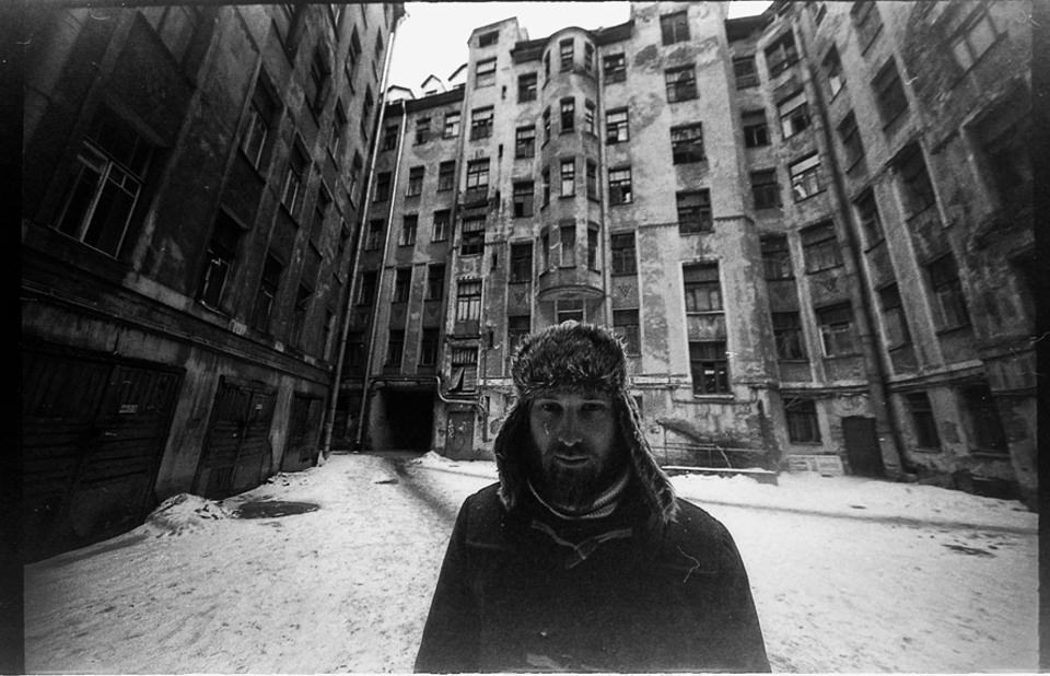 Ein Mann mit Wintermütze steht vor einem verschneiten Gebäude.