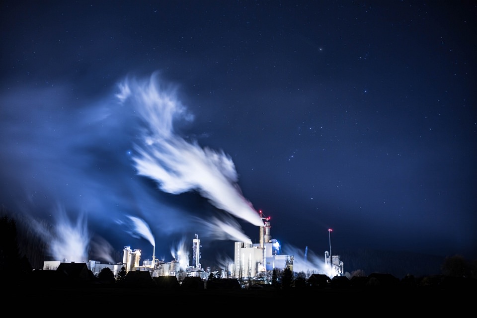 Langzeitbelichtung einer Fabrik mit wehenden Schloten vor dunkelblauem Nachthimmel.