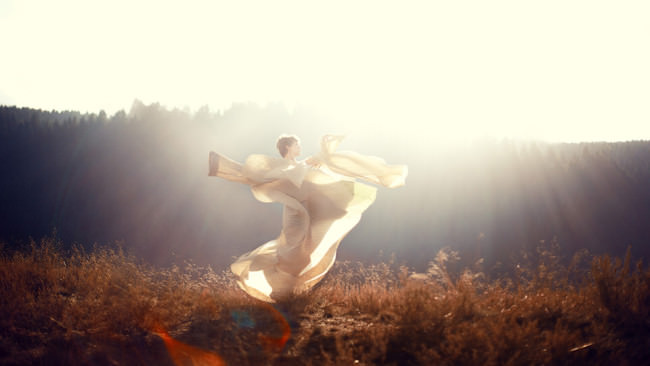 Eine Frau in weißen fliegenden Tüchern im Gegenlicht.