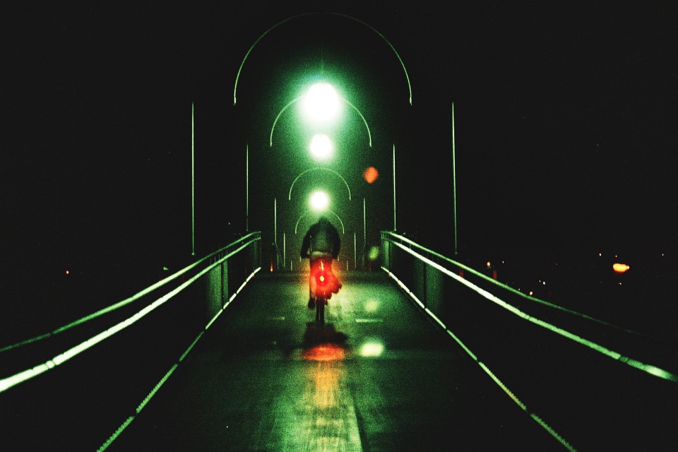 Radfahrer in grünen und roten Lichtern auf einer Brücke in der Dunkelheit.