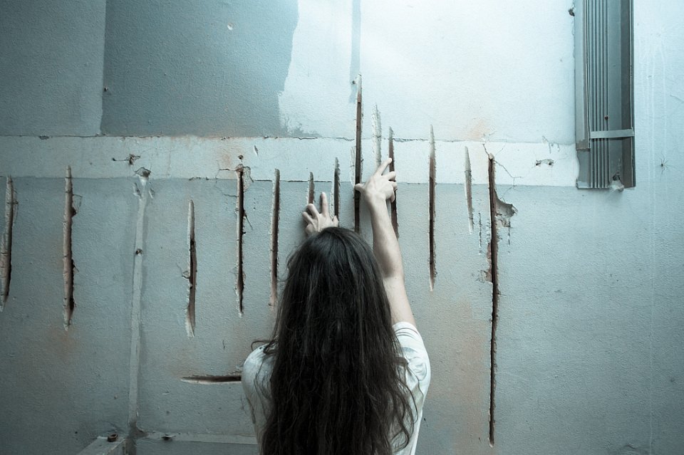 Ein Mädchen fährt mit ihren beiden Händen tiefe Furchen in einer Betonwand nach.