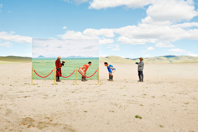 Zwei mongolische Ringer stehen sich mit den Händen auf ihren Knien abstützend gegenüber.