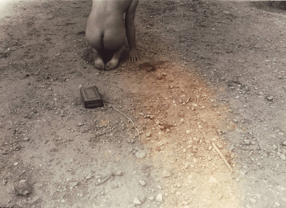 Eine nackte Frau kniet auf dem Boden im Sand.