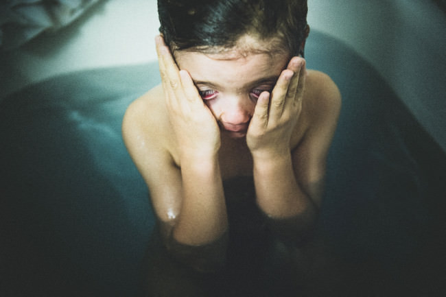 Ein Junge reibt sich die Augen in der Badewanne.