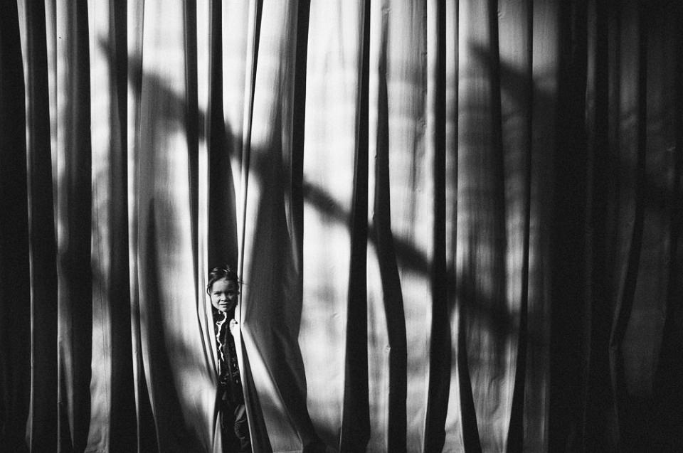 Ein Kind schaut einem sehr großen Vorhang heraus, auf dem Licht und Schatten spielen.