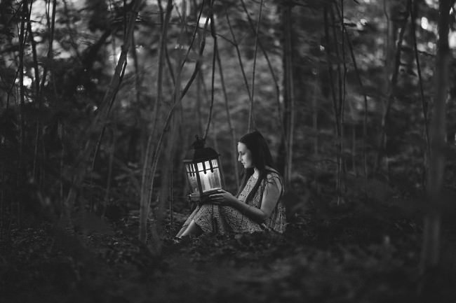 Eine junge Frau sitzt mit einer Laterne im Wald