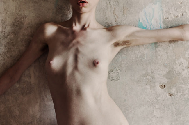 Eine Frau, nackt, barbusig, vor einer Wand.
