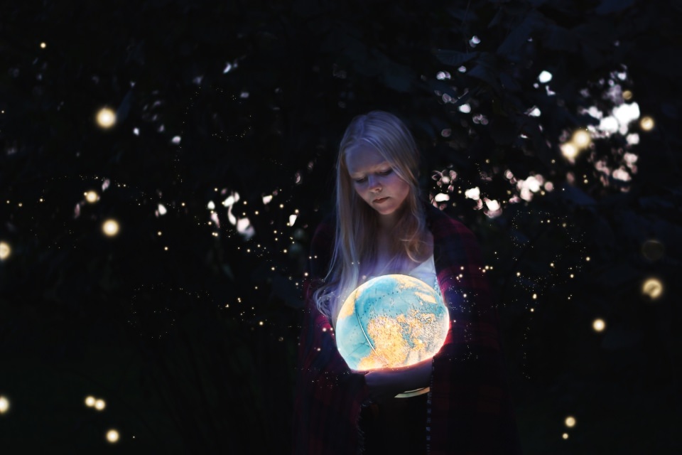 Ein Mädchen hält im Dunkeln einen beleuchteten Globus im Arm, der ihr Gesicht erhellt.