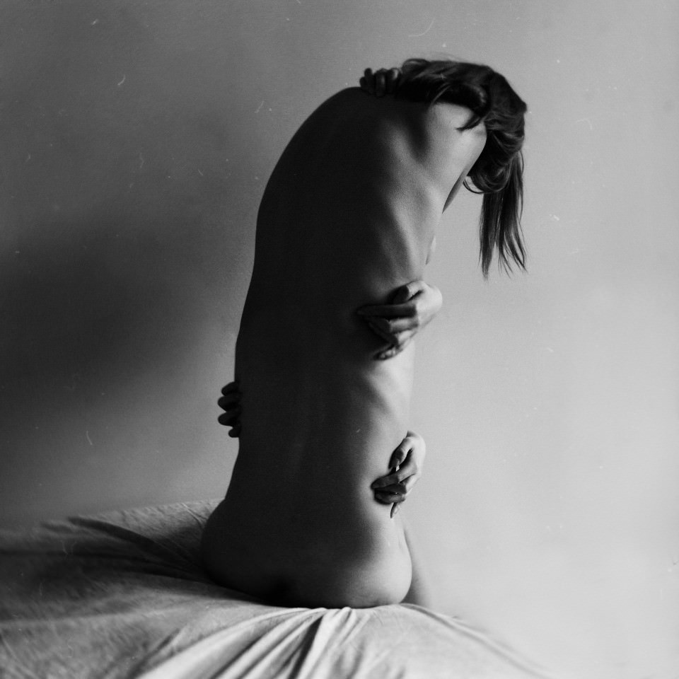 Eine Frau mit drei Händen und gestrecktem Oberkörper sitzt auf einem Bett.