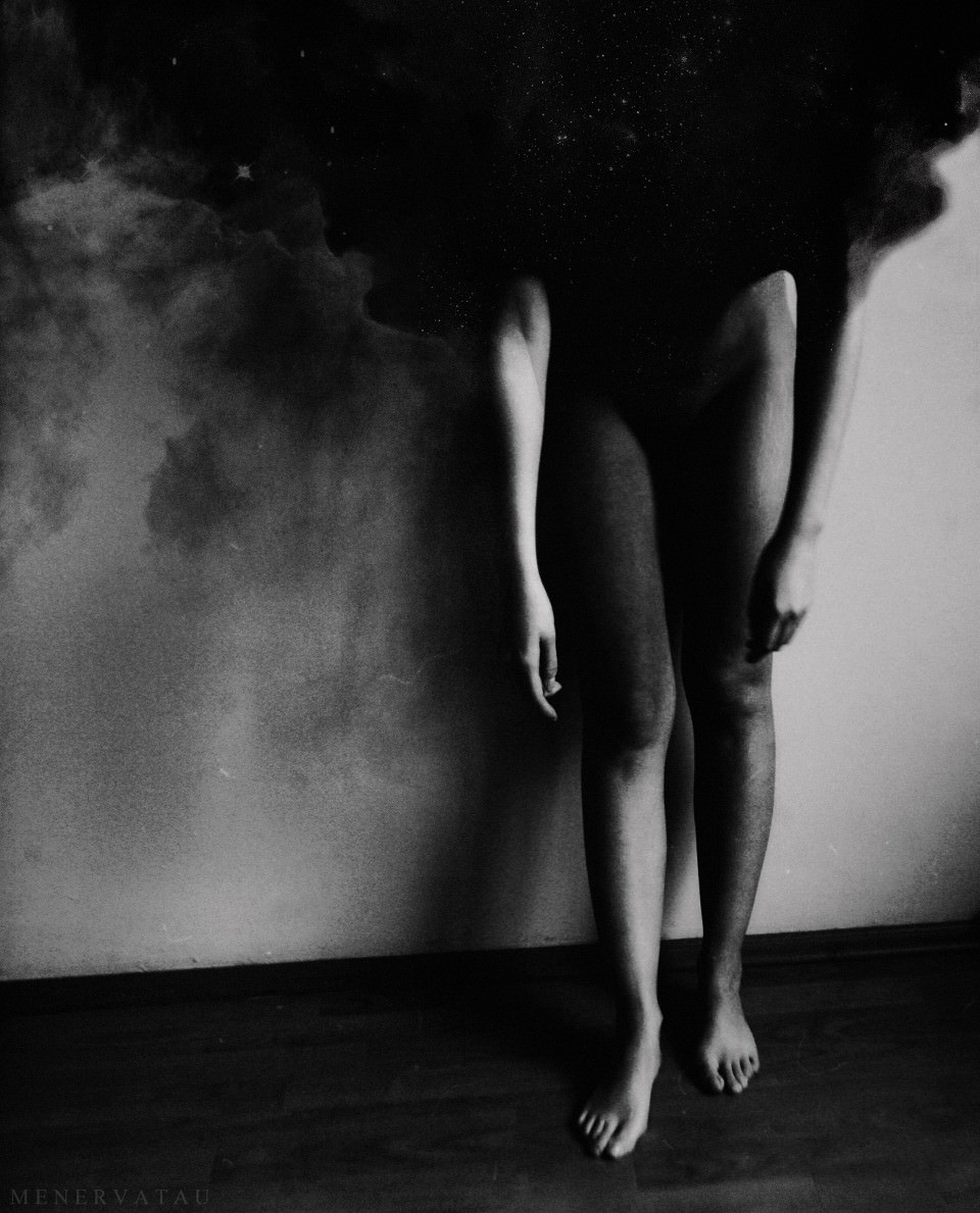 Eine Frau steht vor einer Wand, ihr Kopf löst sich in schwarzen Nebel auf.