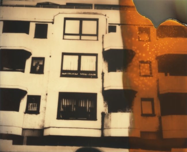 Polaroid einer Hauswand mit orangen Bildfehlern.