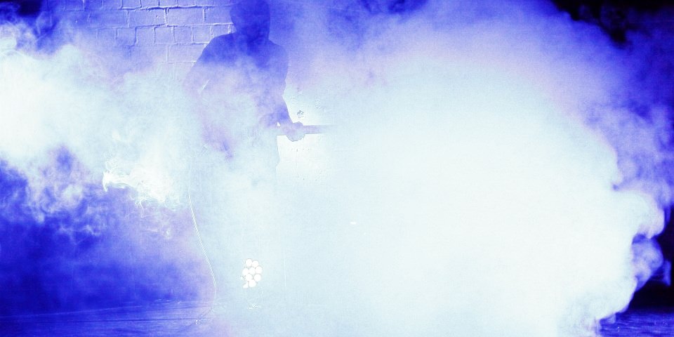 Ein Gitarrist steht fast vollständig von Nebel verhüllt auf einer Bühne.