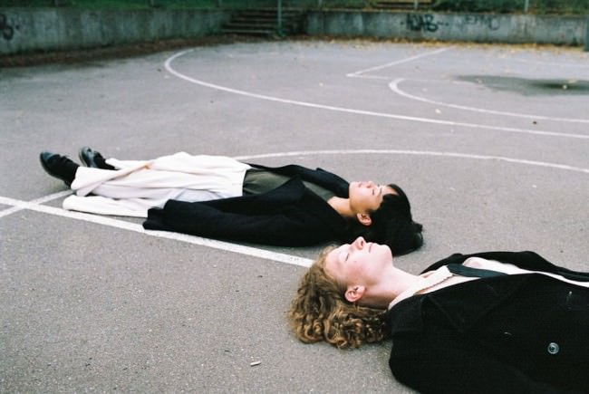 Zwei Menschen liegen auf dem Rücken auf einem betonierten Spielfeld.