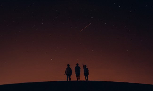 Drei Menschen als Silhouetten am Horizont vor einem Sternenhimmel.