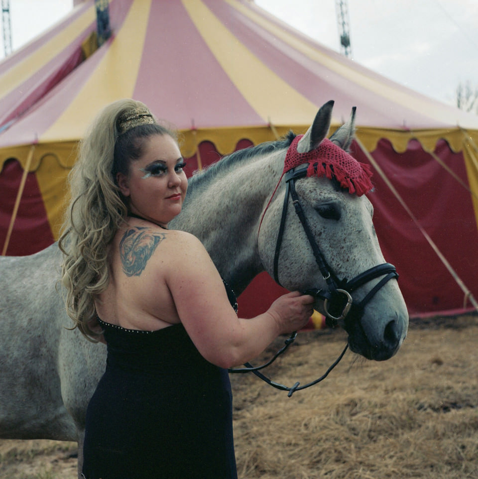 Eine Zirkusfrau steht neben einem geschmückten Pferd.