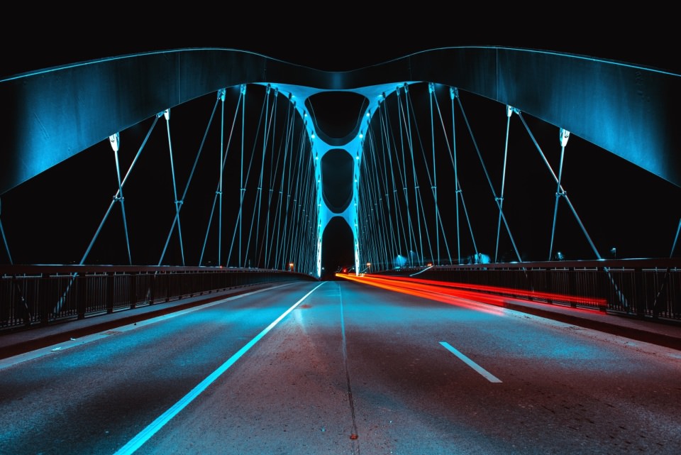 Fahrbahn über eine Brücke, nachts in blauem und rotem Licht.