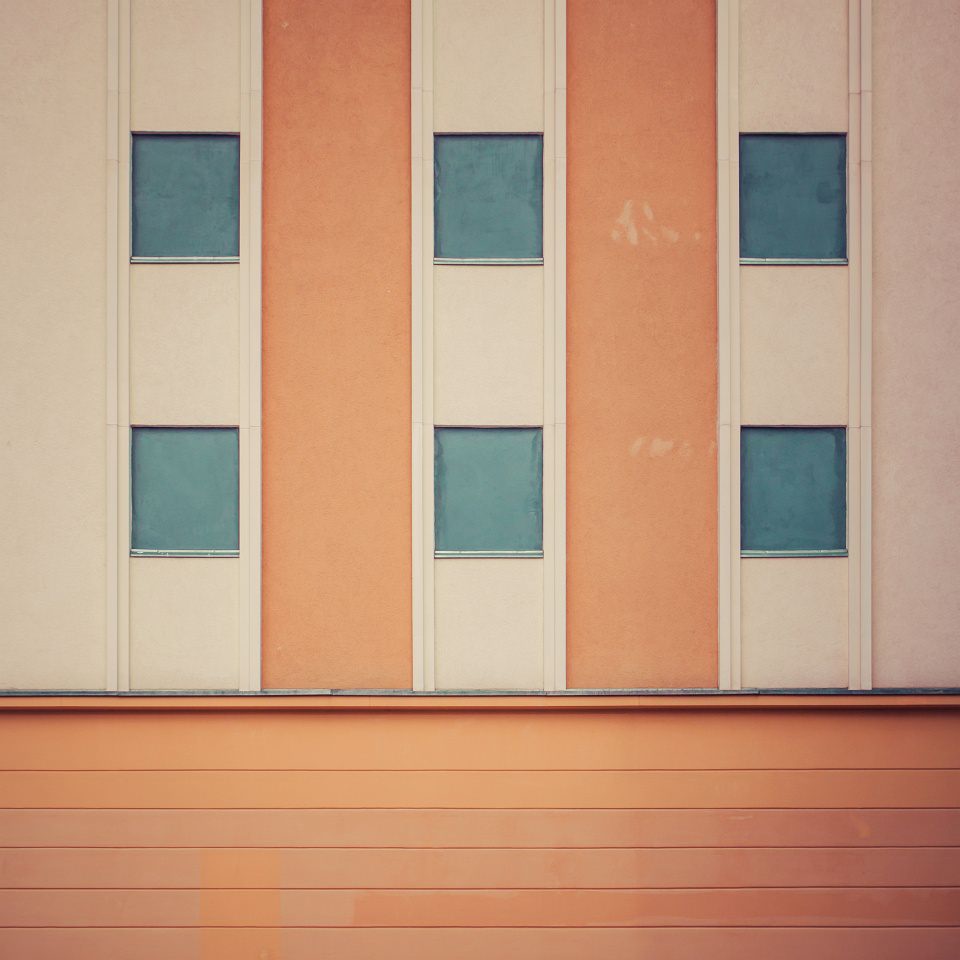Hauswand in orange mit blauen Fenstern.