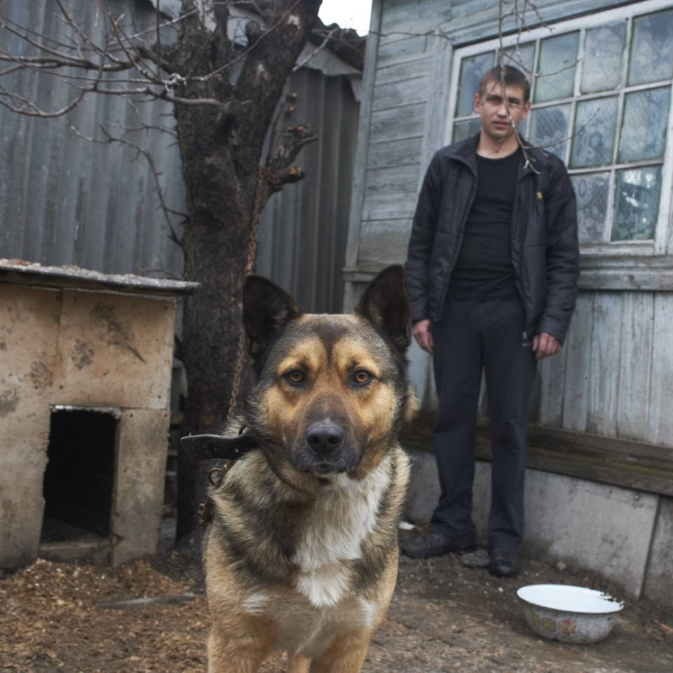 Ein Hund an der Kette vor seiner Hütte, mit seinem Besitzer.